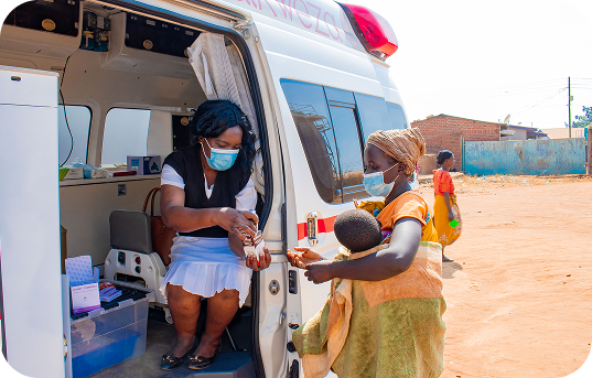 A Wandikweza health worker assisting a mother and child at a mobile clinic van